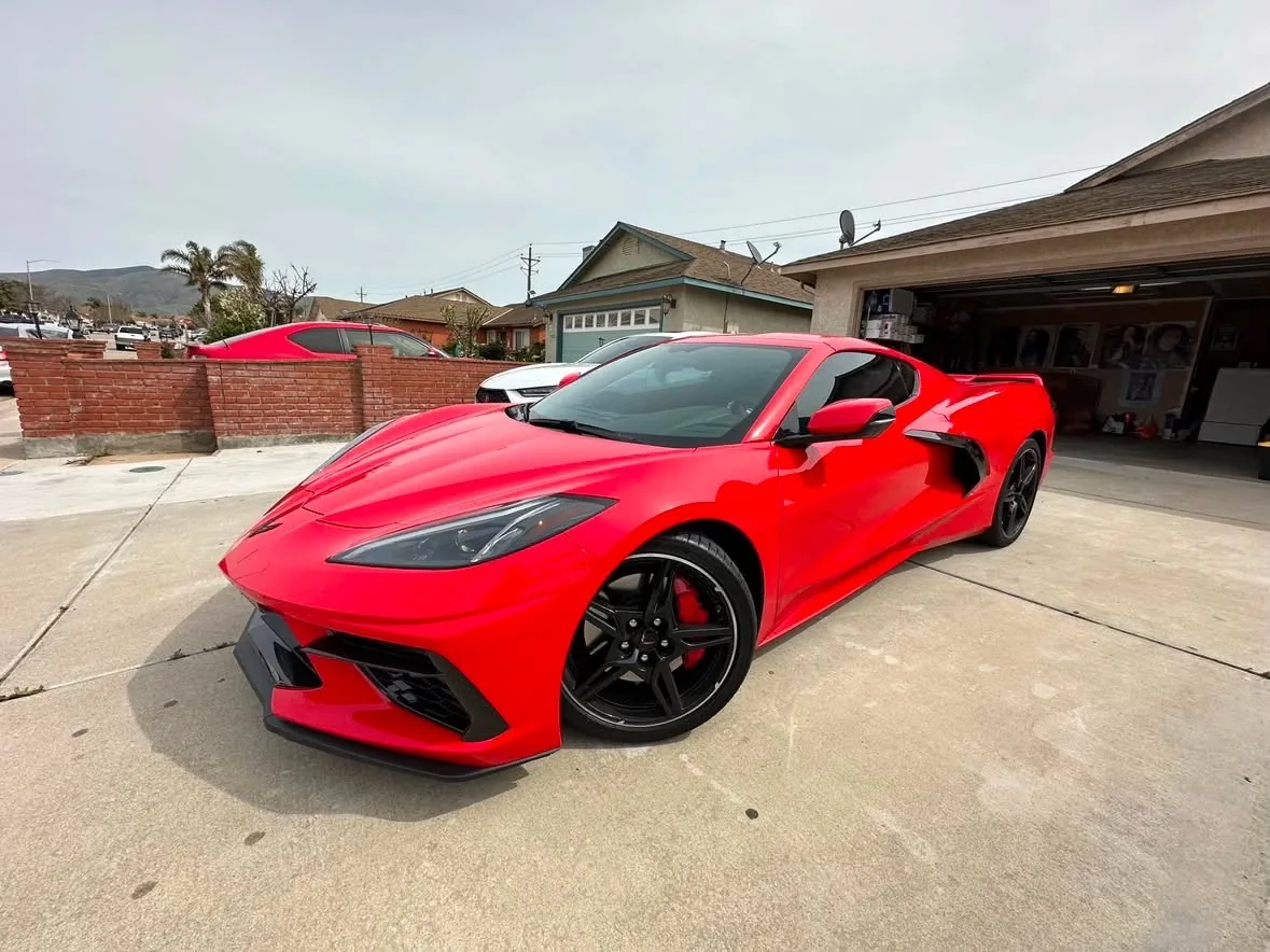 A red mid engine Chevrolet Corvette in a driveway, film on the door and quarter glass