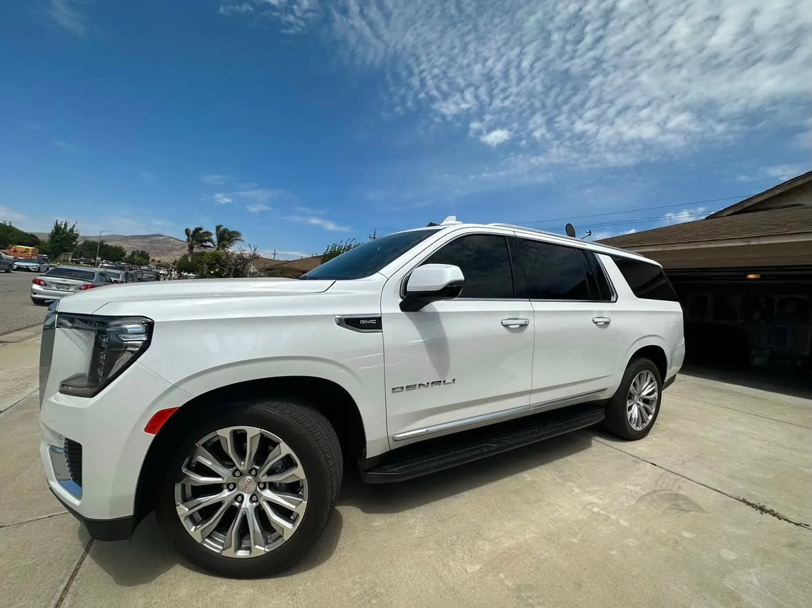 A white GMC Yukon Denali with the front windows tinted to match the rear glass